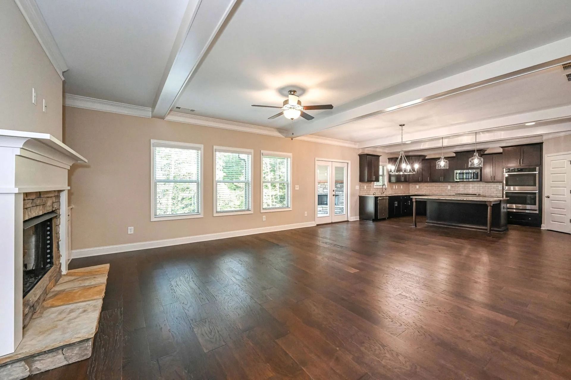 Open-concept living space with a fireplace, windows, and a kitchen with dark cabinets and an island.