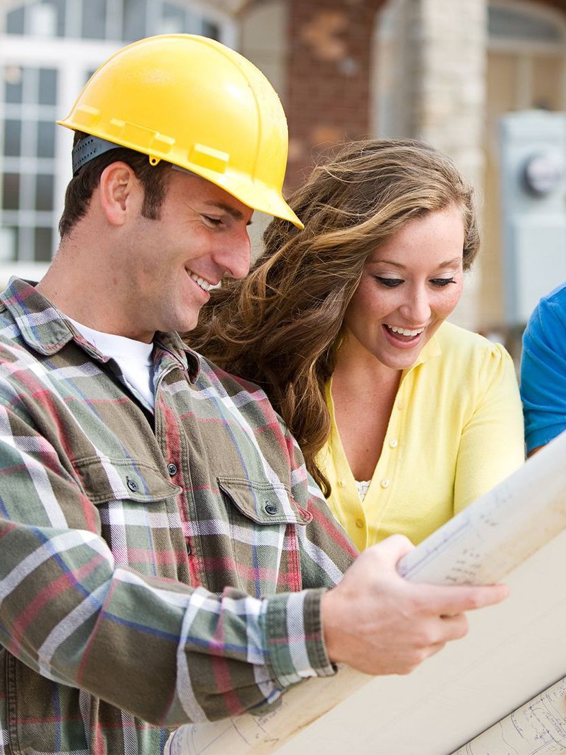 Construction worker and woman looking at blueprints, smiling, outdoors.