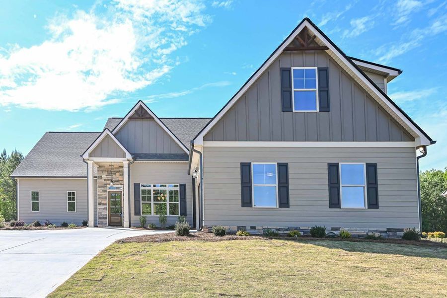 A two-story house with gray siding, a gabled roof, and a driveway under a blue sky.