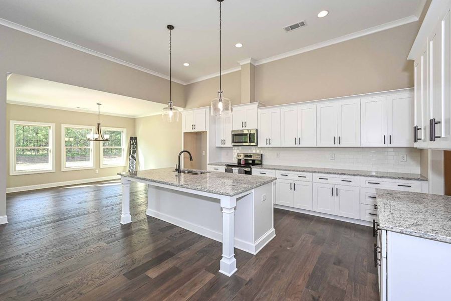 Bright, modern kitchen with white cabinets, island, and dark wood floors. Dining area visible in the background.