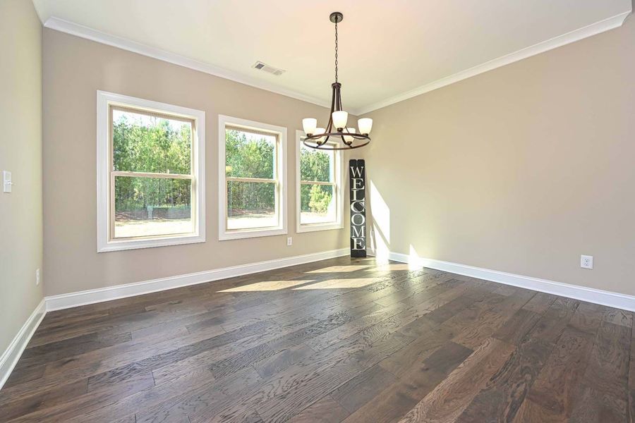 Empty dining room with hardwood floors, three windows, and a chandelier.