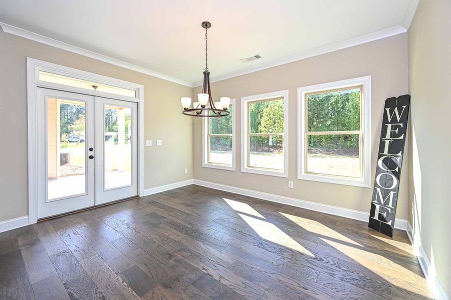 Dining room with dark wood floor, three windows, french doors, and welcome sign.
