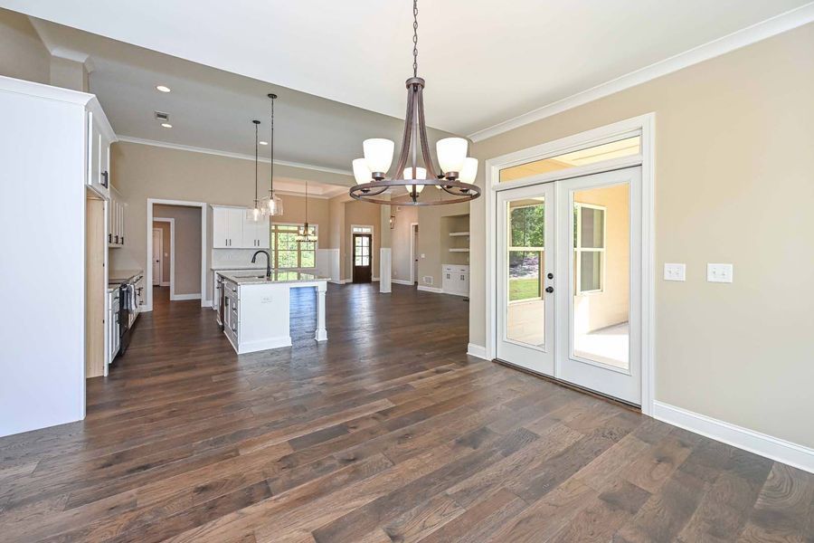Spacious interior with hardwood floors, kitchen island, and French doors. Neutral walls, white trim, and a chandelier.
