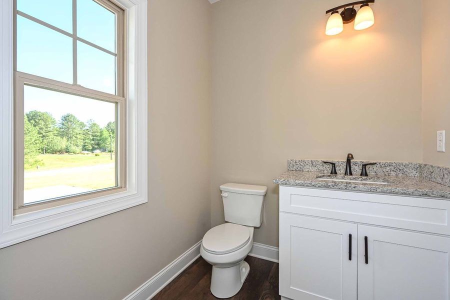 Powder room with a toilet, sink, and window. Beige walls, white vanity, and granite countertop.