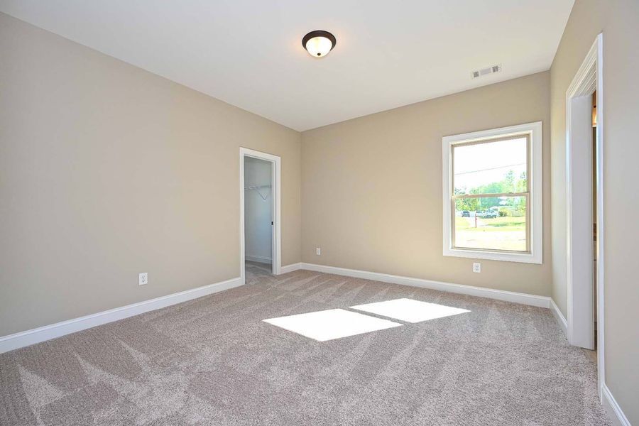 Empty bedroom with beige walls, carpet, window, and doorway.