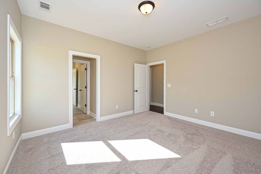 Empty beige bedroom with carpet, doorway, and natural light.