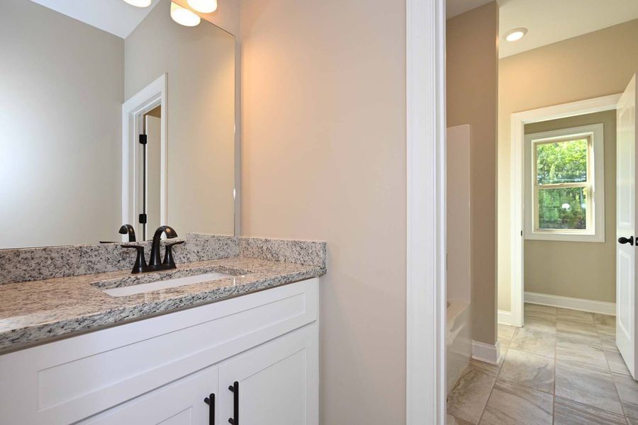 Bathroom with white vanity, granite countertop, and doorway to a room with a window.