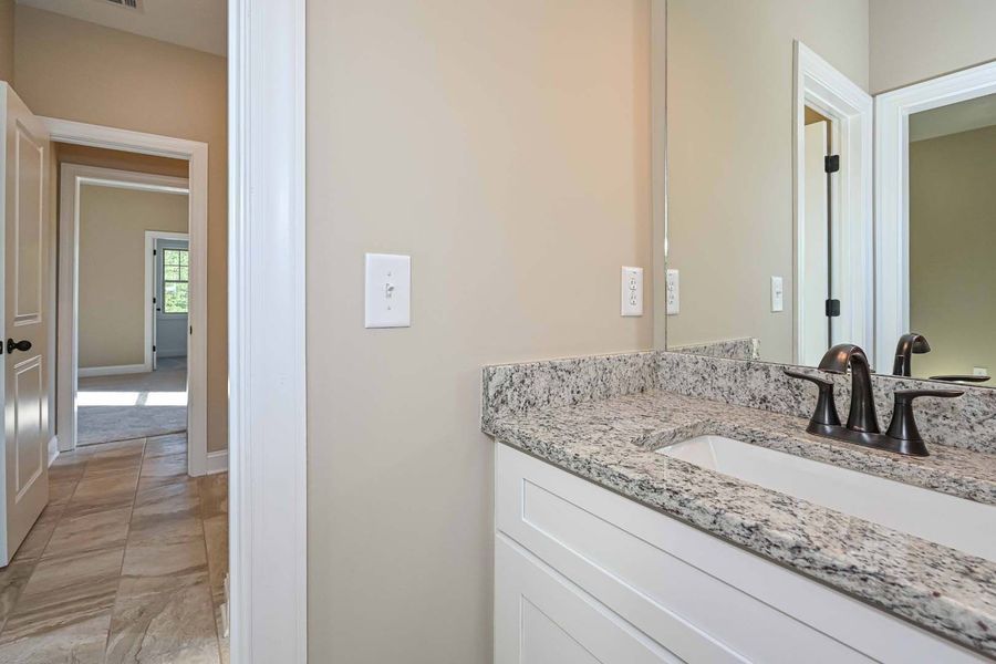 Bathroom with granite countertop vanity, mirror, and doorway to hallway.