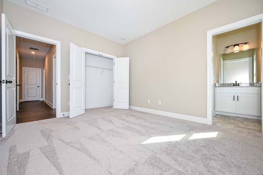 Empty bedroom with neutral carpet, closet, and doorway to a bathroom.