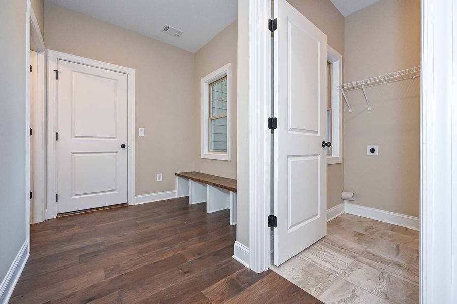 Laundry room with white doors, wood bench, and wood and tile floors.