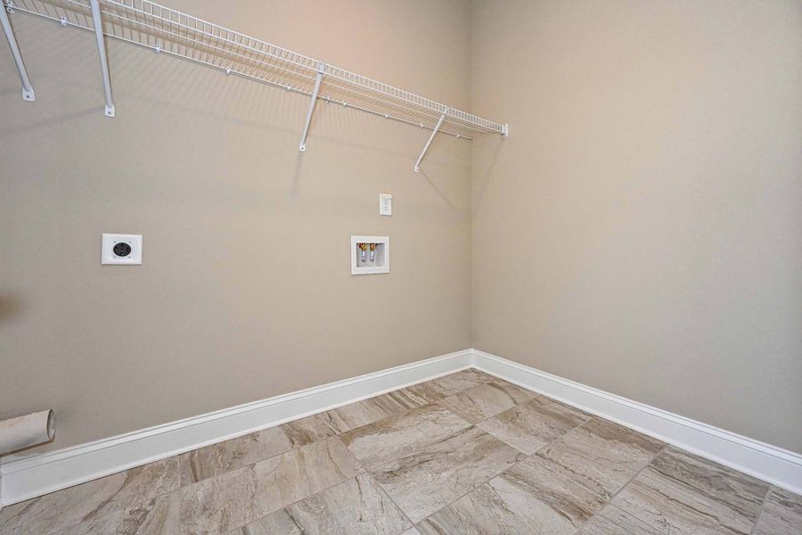 Empty laundry room with beige walls, tiled floor, wire shelving, and washer/dryer hookups.
