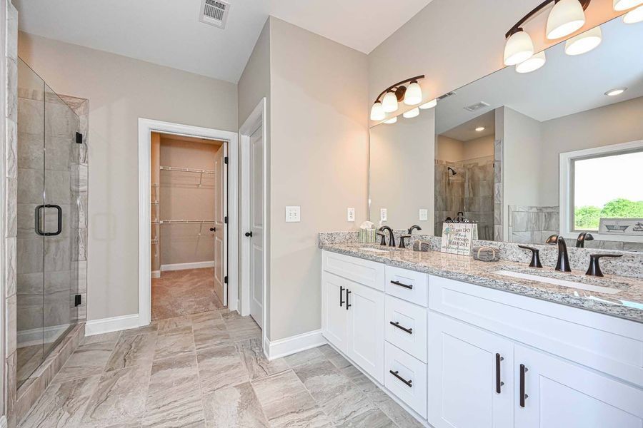 Bathroom with white double vanity, gray countertops, glass shower, and walk-in closet.