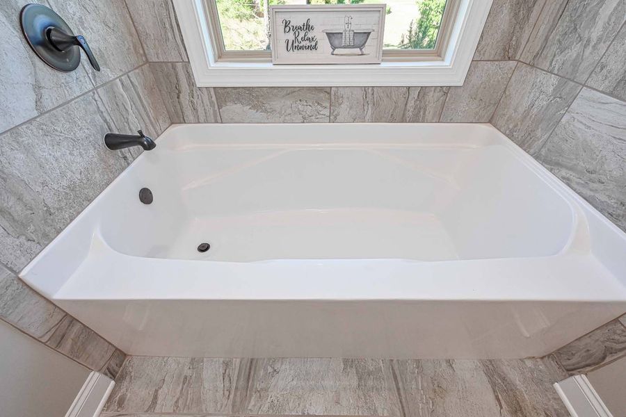 White bathtub beneath a window, surrounded by tiled walls. Black faucet and decor.