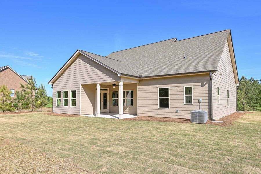 Back view of beige house with a patio, green lawn, and a clear blue sky.