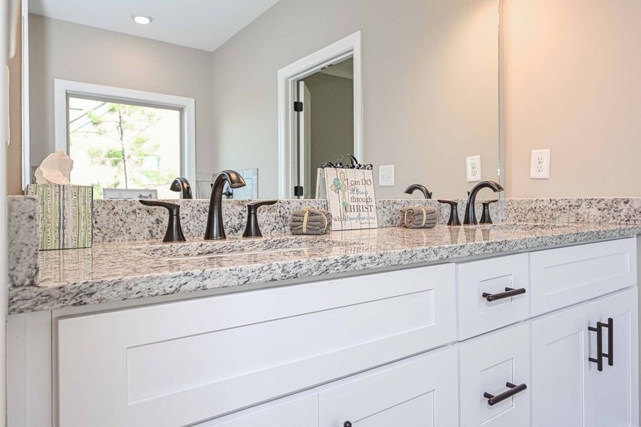 White bathroom vanity with granite countertop, black fixtures, and large mirror.