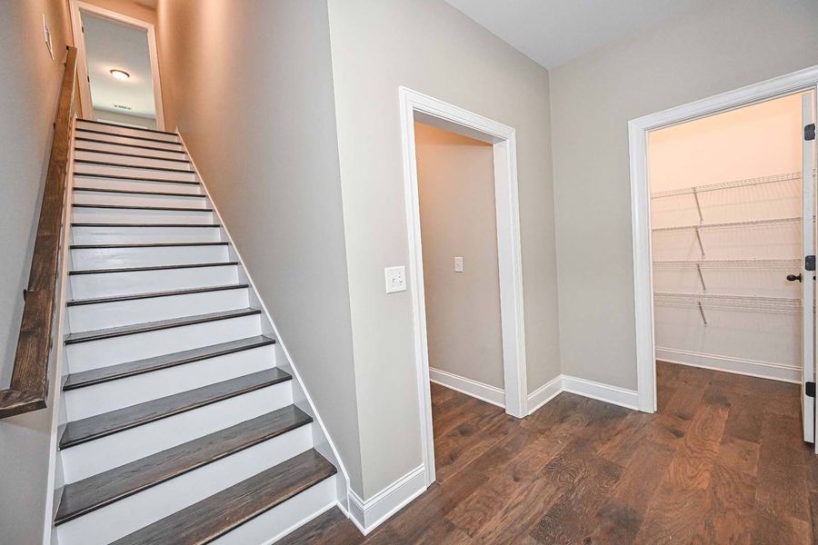 Staircase leading to a second floor, next to a hallway with doors and a pantry.