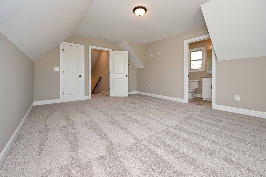 Beige carpeted room with angled walls, doors, and a bathroom visible in the background.