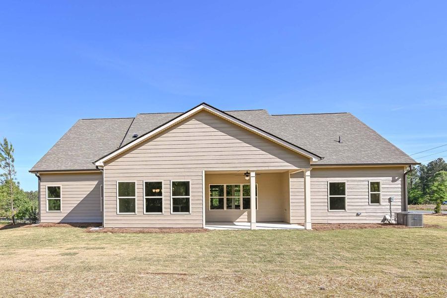 Rear view of a beige house with a covered patio, set against a blue sky.