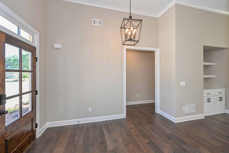 Entryway with dark wood floors, beige walls, a wooden door, and a hanging light fixture.