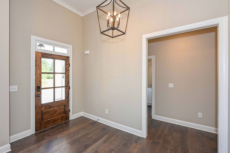 Entryway with wooden door, dark floors, beige walls, white trim, and a hanging lantern.