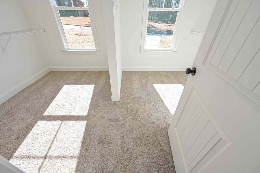 Empty carpeted room with white walls and windows, sunlight streams in.