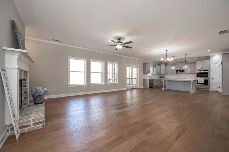 Open-concept living space with fireplace, kitchen, and windows; hardwood floors, light gray walls, and bright natural light.