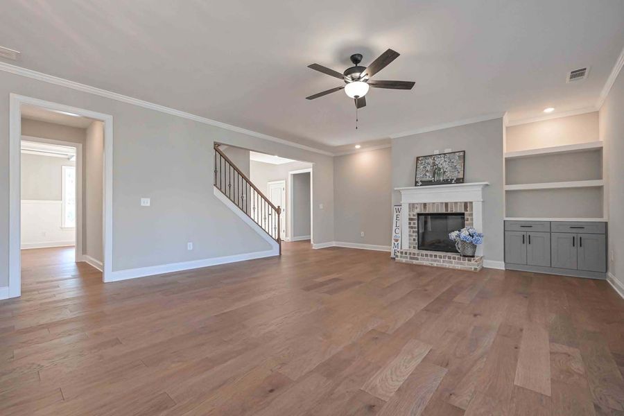 Empty living room with hardwood floors, fireplace, built-in shelves, and a staircase.
