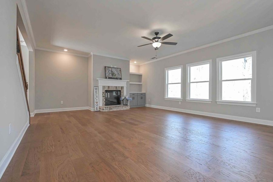 Empty living room with hardwood floors, fireplace, and three windows.