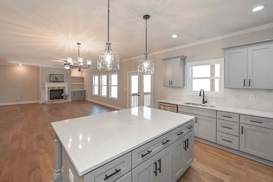 Modern kitchen with gray cabinets, white countertops, island, and view to living room.