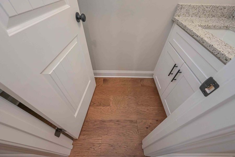 Narrow bathroom doorway with white door and vanity; hardwood floors, light gray wall.