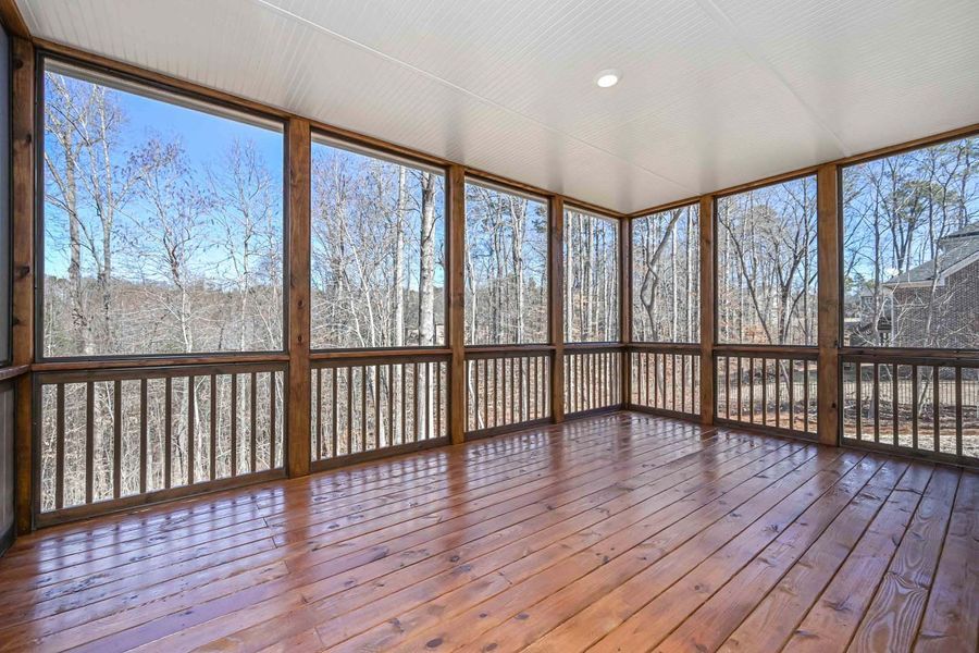 Screened porch with wooden floor, railing, and surrounding view of trees under a blue sky.