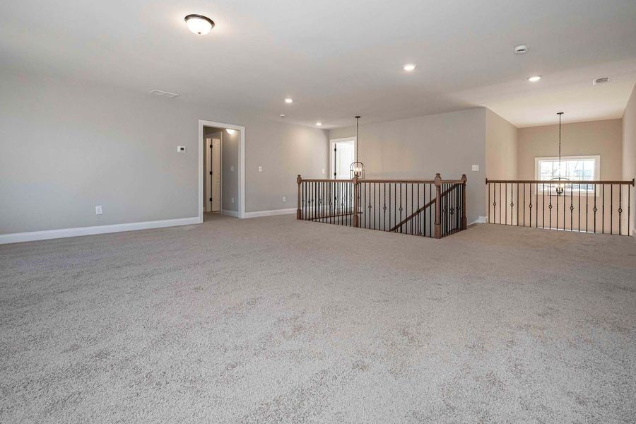 Empty, carpeted loft with a railing, neutral walls, and recessed lighting.