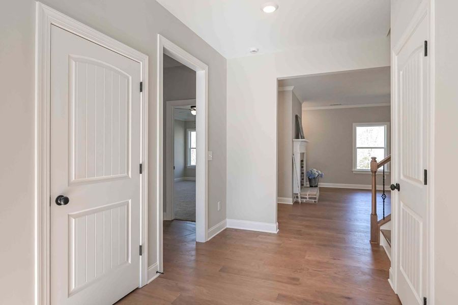 Hallway with hardwood floors, white doors, and a view of a living room.