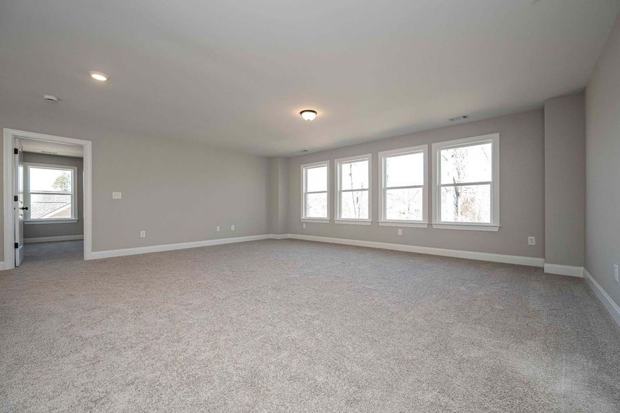 Spacious, empty room with gray carpet, light gray walls, and multiple windows.