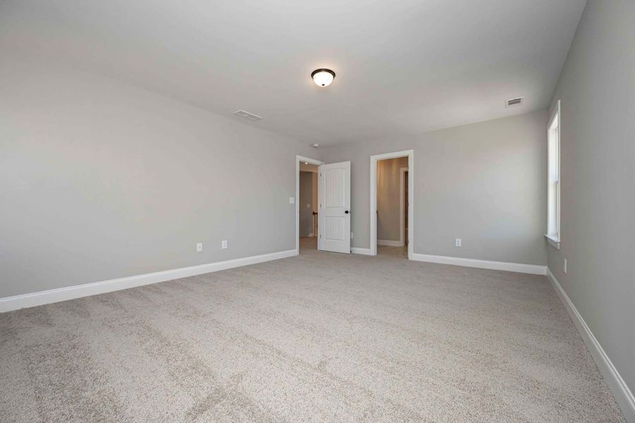 Empty bedroom with gray walls, beige carpet, and three doorways.