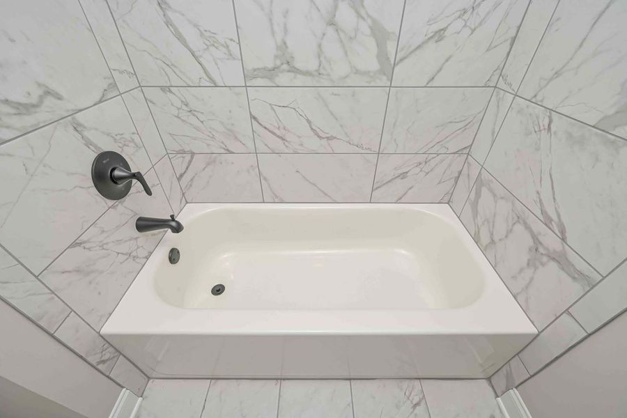 White bathtub surrounded by marble-patterned tile, black faucet, in a bathroom.