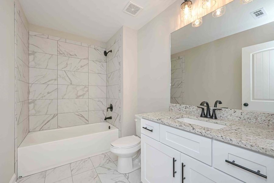 White bathroom with marble tile, vanity, toilet, and tub.