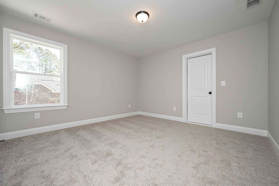 Empty bedroom with light gray walls, white door and window, and gray carpet.