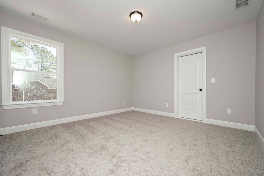 Empty bedroom with grey walls, carpet, white door, and a window.