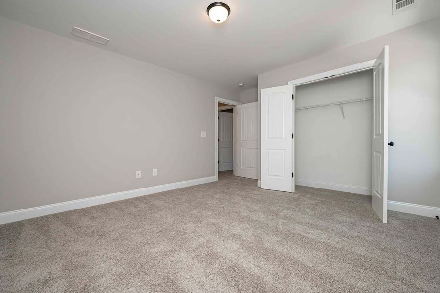 Empty bedroom with gray walls and carpet, a closet, and a doorway.