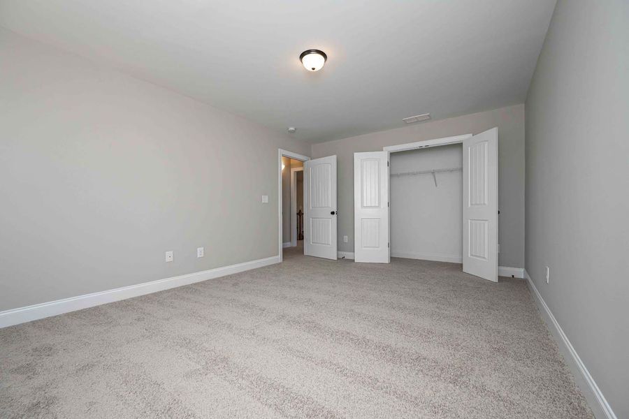 Empty bedroom with gray walls, carpet, closet, and door.