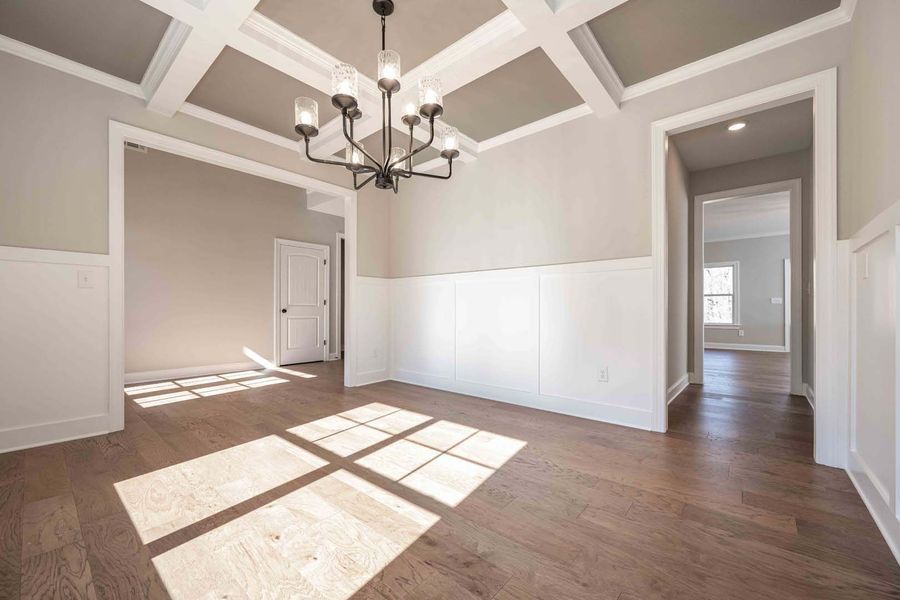 Empty dining room with wood floor, white trim, and chandelier; sunlight streams in.