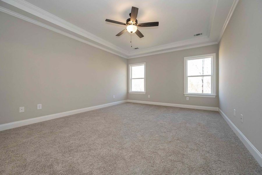 Empty bedroom with light gray walls, carpet, and two windows; a ceiling fan is centered.
