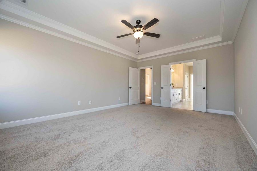 Empty bedroom with light gray walls, carpet, and a ceiling fan. Two doors lead to a bathroom.