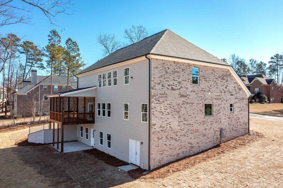 Three-story house with gray siding, brick accents, and a wooden deck under a blue sky.