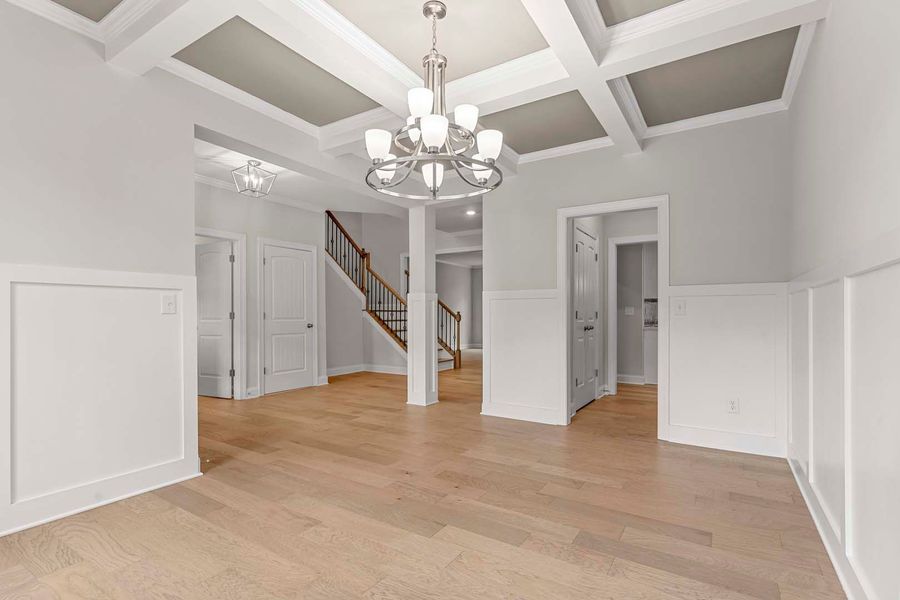 Spacious dining room with light wood floors, white walls, coffered ceiling, and a chandelier.