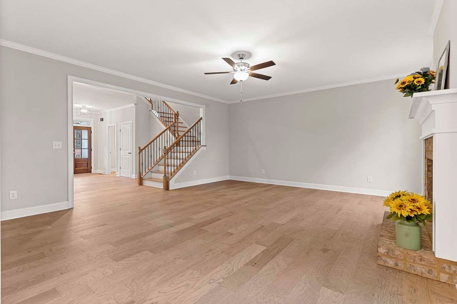 Empty living room with light wood floors, stairs, and a fireplace.
