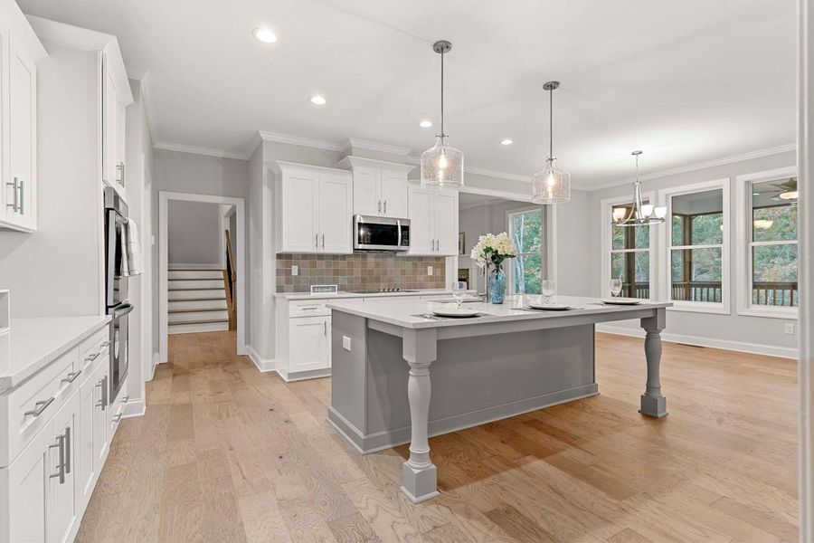 Spacious, bright kitchen with a gray island, white cabinets, and light wood floors.