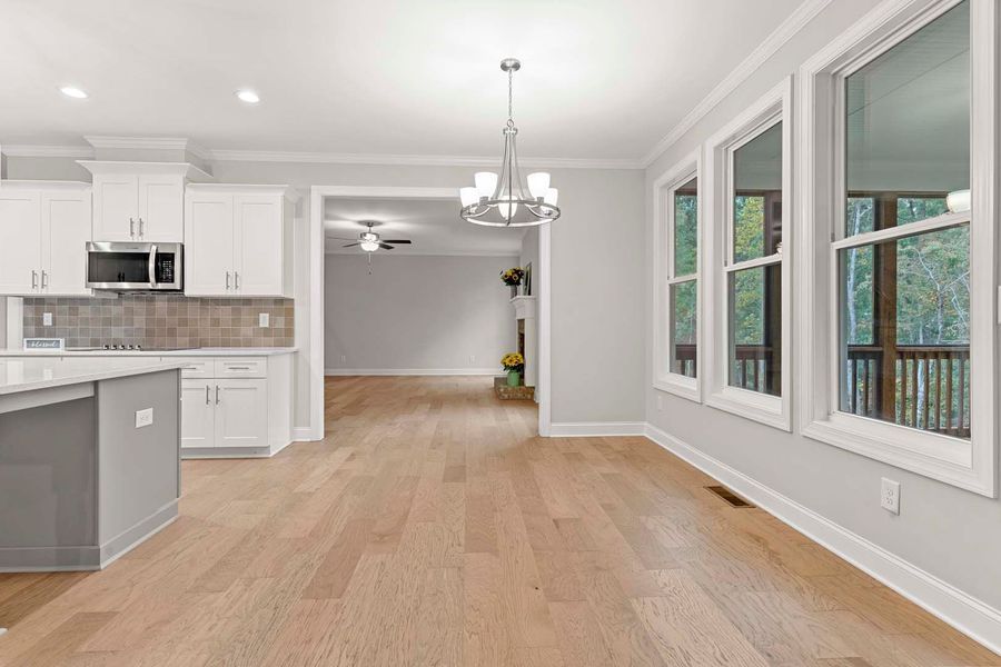 Bright kitchen with white cabinets, island, and light wood floors, leading into a living area.