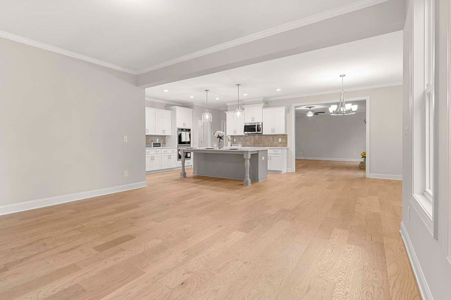 Open-concept living space with light wood floors, white kitchen, gray island, and neutral walls.
